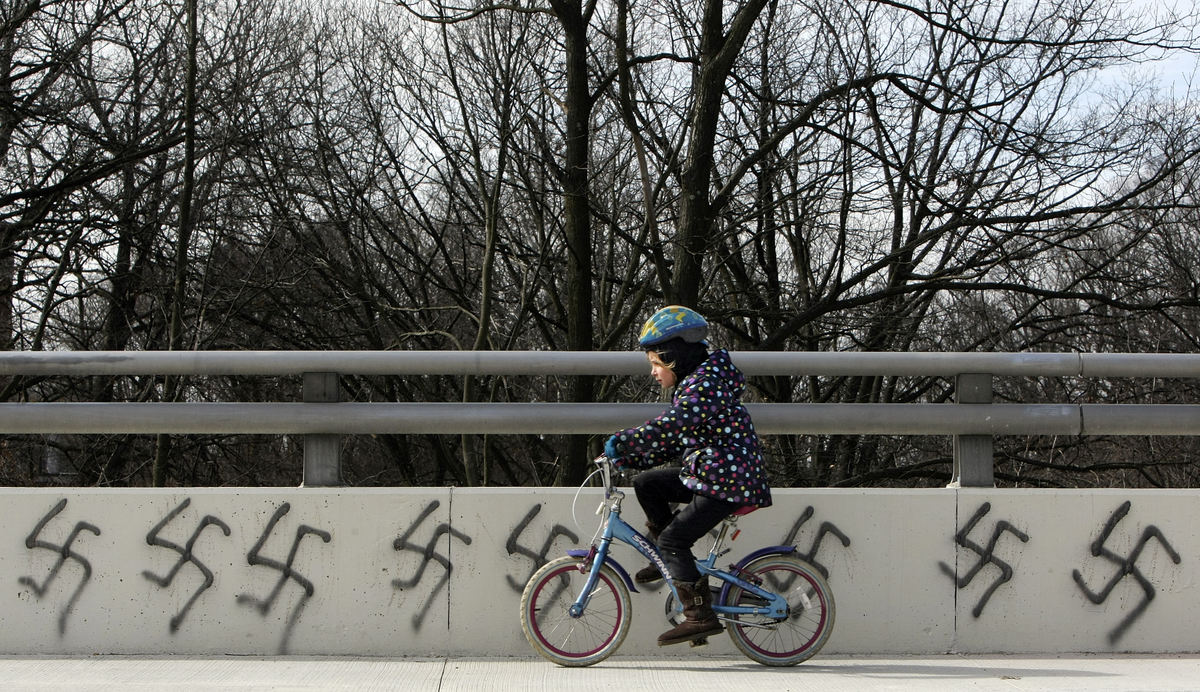 General News - 1st placeSummer Dush, 7, rides by graffiti of swastikas painted on the bridge on Calumet Street between Olentangy Street and Arcadia Avenue in Clintonville. Graffiti was painted on garage doors and store walls in and around Clintonville, late last night or early this morning. (Neal C. Lauron / The Columbus Dispatch)