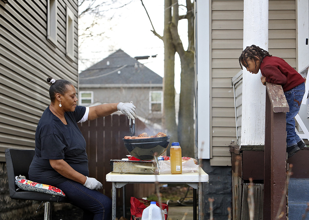 Felicia Jackson grills outdoors for the first time at her daughters Teresa Jackson's Columbus home while grandson Kahleel Jackson watches from the porch . (Eric Albrecht / The Columbus Dispatch)