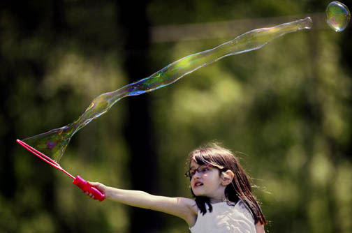 Feature - HM - Backlit by a seldom seen sun, Madison Tibbals creates a long soap bubble while playing at Highbanks Metro Park with her mother Halli and little sister Hayden, 3. (Chris Russell / The Columbus Dispatch)