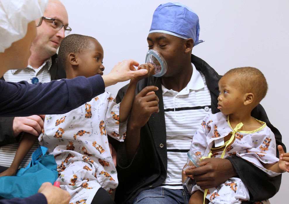 Story - 1st placeChild life specialist Michelle Peterson (left) places an  anaesthesia mask over the mouth and nose of interpreter Denso Gay to demonstrate to Elie Pierre (left) held by hospital medical photographer Ted Stevens, and Kurtis Petion how the mask will be placed on them before their surgeries at the hospital in Akron.   (Karen Schiely / Akron Beacon Journal)