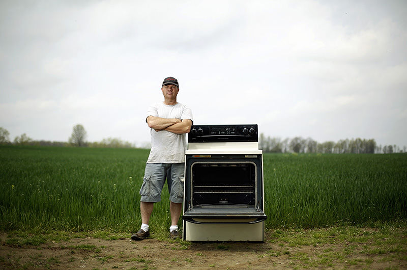 Portrait - 3rd place - Daniel George of Forest, Ohio stands next to his broken stove in his yard after a power surge in 2014 fried almost all of his appliances in his home.  George lost more than $4,500 worth of appliances and AEP refused to pay for the damage, so he filed a complaint with the state.  The state said AEP is not liable for malfunctioning AEP equipment.   (Kyle Robertson / The Columbus Dispatch)