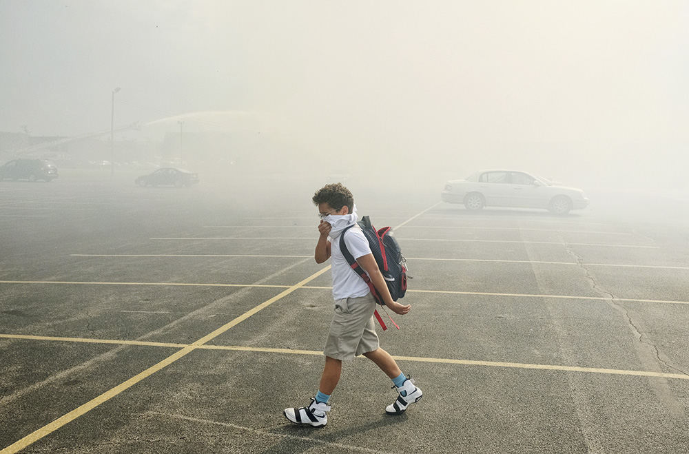    Spot News - 1st place - Cameron Walker walks through the parking lot at St. Patrick's of Heatherdowns and shields himself from the smoke coming from the fire at the Andover Apartments in Toledo.  (Jeremy Wadsworth / The (Toledo) Blade)