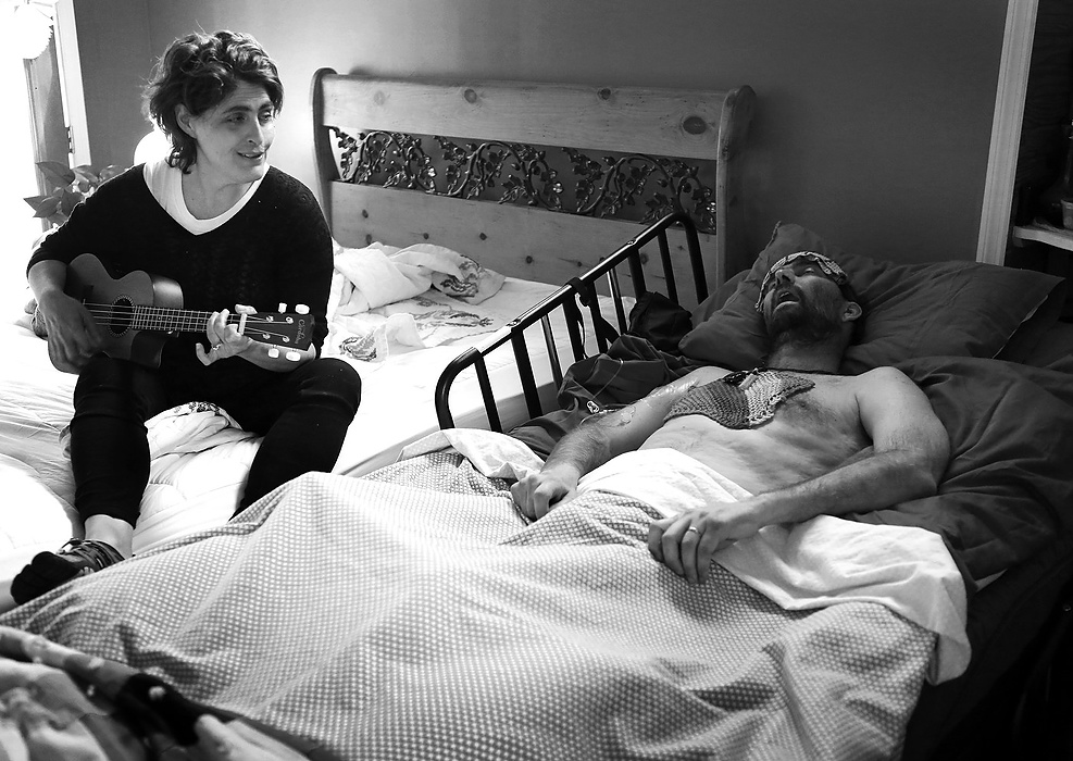 First Place, Photographer of the Year - Large Market - Carrie Cochran / Cincinnati EnquirerApril 23, 2015: In Joe Neyer's final hours, his wife Laurie sings, "Dirty Knees," a song she wrote about him. Two and a half years earlier, Neyer was diagnosed with glioblastoma multiforme, the most aggressive form of brain cancer. Months after his diagnosis, he decided that he will not get treatment. "By accepting death, you can actually enjoy life," he said. 