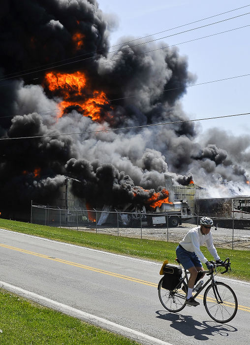 Spot News - 2nd placeA bicyclist rides past a fire at the RD Holder Oil Co. in rural Clark County. The fire, which started when a tanker truck caught fire near the companies warehouse, quickly engulfed the entire business. Fire fighters battled the blaze for more than six hours. (Bill Lackey / Springfield News-Sun)