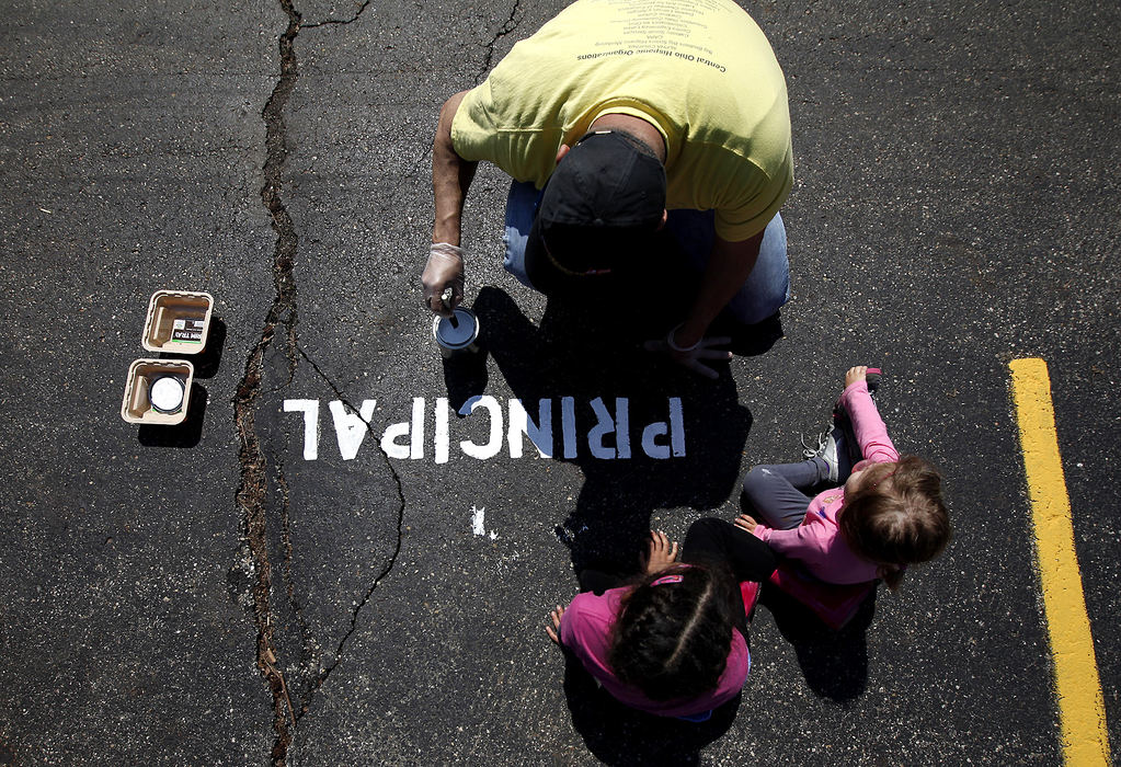 General News - 1st place - Volunteer Rick Perez of Westerville puts the finishing touches on a reserved parking space for Principal Jeni Quesenberry as sisters Karina and Sofia Pantoja, of Polaris, watch at Parkmoor Elementary School in Columbus. Parkmoor was one of the locations picked by Vineyard Columbus to get a spring makeover as part of the church's Serve Columbus initiative. Vineyard, along with volunteers from Keep Columbus Beautiful, the Columbus Shelter Board and local residents partnered for the day of service event. (Sam Greene / The Columbus Dispatch)