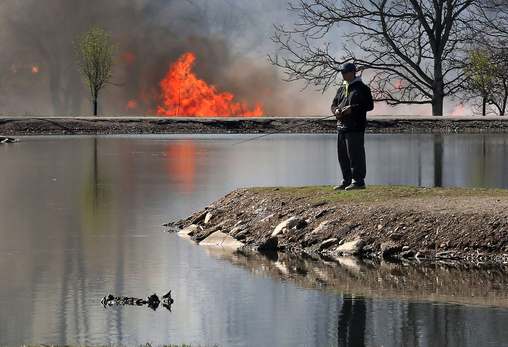 Feature - 1st place - A fisherman takes advantage of the warm weather and sunshine at Old Reid Park while a field fire rages across the lake. The fire was a controlled burn by National Trail Parks and Recreation who were burning the tall grass in the Kirby Preserve.  Bill Lackey / Springfield News-Sun