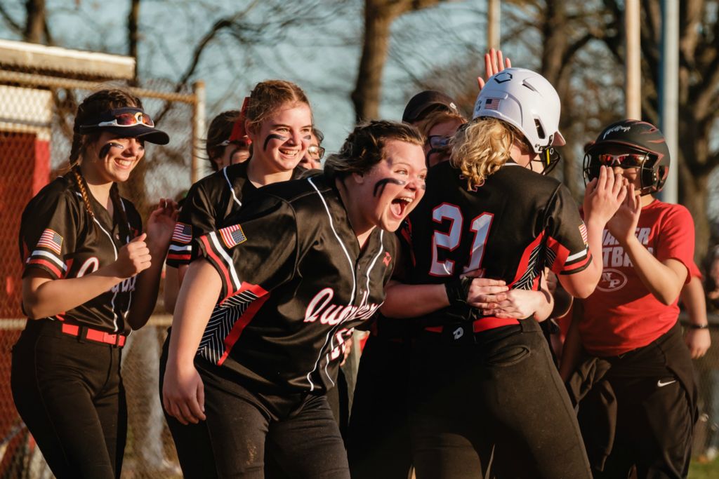 Sports Feature - HM - After crossing home plate to score the winning run in the 10th inning against Dover, New Philadelphia’s Ellie Mason celebrates with starting pitcher Julia Miller (center), Miller threw 141 pitches in 10 innings for a 2-1 victory.  (Andrew Dolph / The Times Reporter)