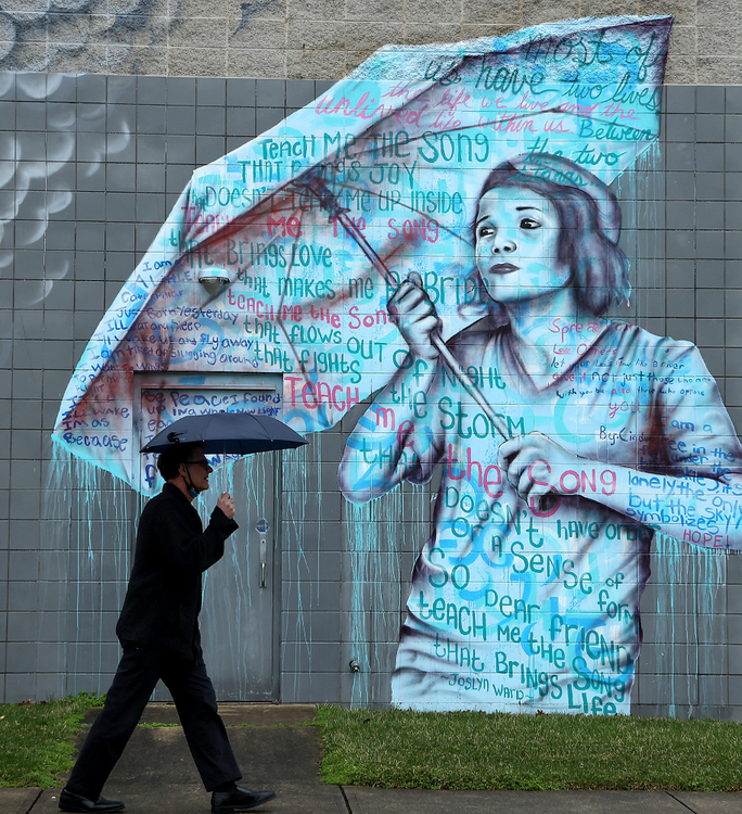 Feature - 3rd place - A man walks past the mural on the side of the Springfield YMCA in the rain with an umbrella. (Bill Lackey / Springfield News-Sun)