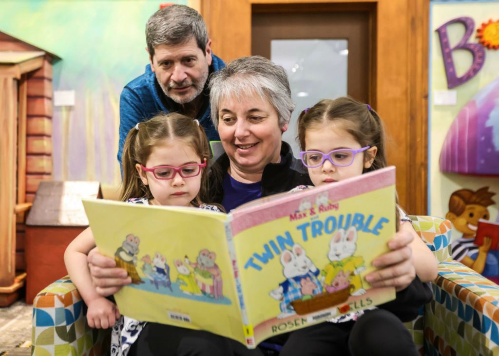 Feature - HM - Oregon resident Judy Zbierajewski (center) reads a book to granddaughters Cora (left) and Adeline Taylor, both 4, to escape an overcast day while babysitting the twins with Don Zbierajewsk at Toledo Lucas County Public Library. (Isaac Ritchey / The Blade)