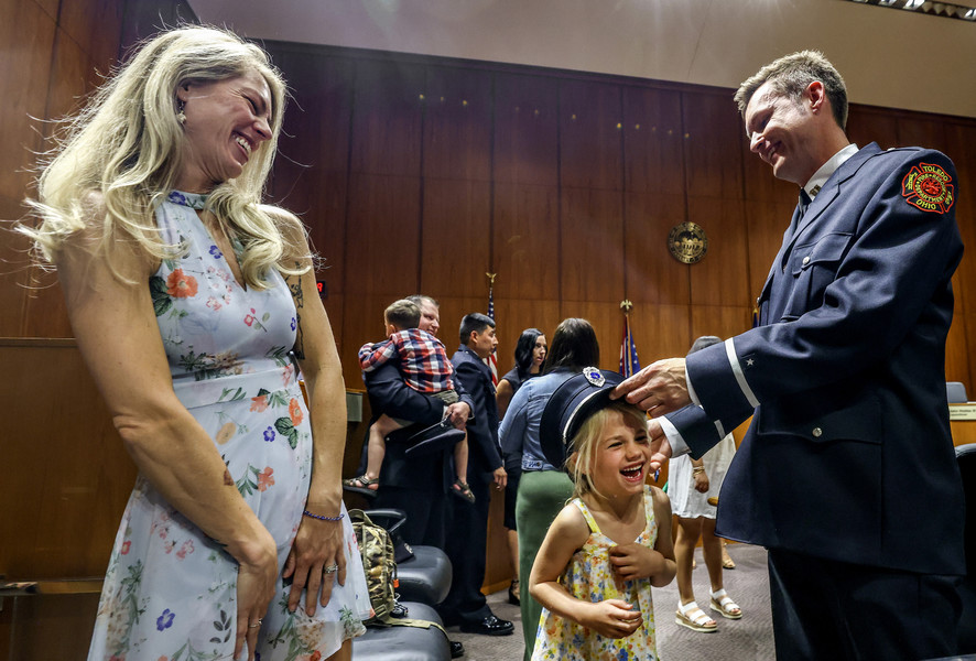 General News - 1st place - Coraline De Saint Victor, 5, tries on her father Colin De Saint Victor’s hat after he is promoted to Captain in the Toledo Fire & Rescue Department at One Government Center in Toledo. Mr. De Saint Victor’s wife Kadie (left) watches the fun.  (Jeremy Wadsworth / The Blade)