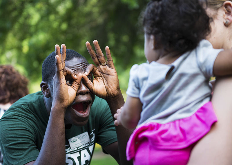 Feature - 1st place - Henry Boachi (left) a graduate student from Ghana, makes a funny face for Annika Braimah, 7 months, as she is held by her mother Shannon Braimah at the International Student Picnic held at Richland Avenue Park in Athens.  (Isaac Hale / Ohio University)