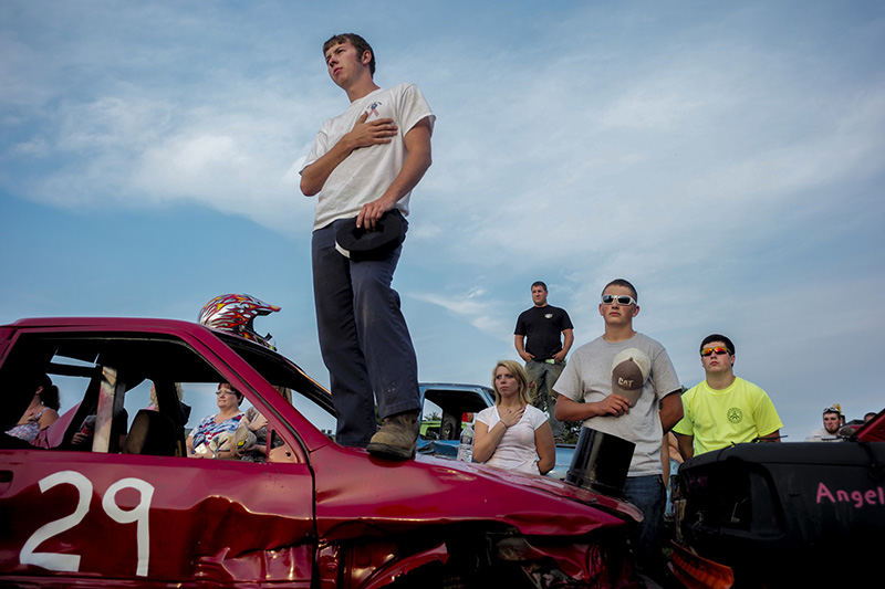 Sports Feature - 1st place - Tommy Smith, 19, of Johnstown, stands on his derby car during the playing of the national anthem before the start of the demolition derby at the Hartford Fair in Licking County. (Joshua A. Bickel / ThisWeek Community News)