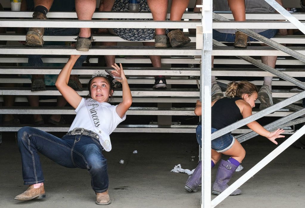 Story - 3rd place - Peightyn Linton, 11, of Fremont (left) and her cousin McKenna Johnson, 5, slide under the stands in the dairy barn to retrieve dropped sunglasses during the first day of the Sandusky County Fair in Fremont.  Jeremy Wadsworth / The Blade