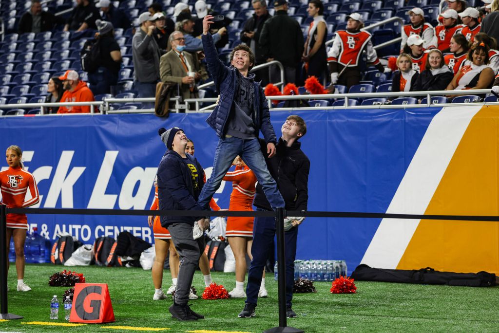 Feature - HM - A Bowling Green fan uses his friends as a boost to take a selfie with the BGSU band before the start of the 2022 Quick Lane Bowl at Ford Field in Detroit. (Rebecca Benson / The Blade)