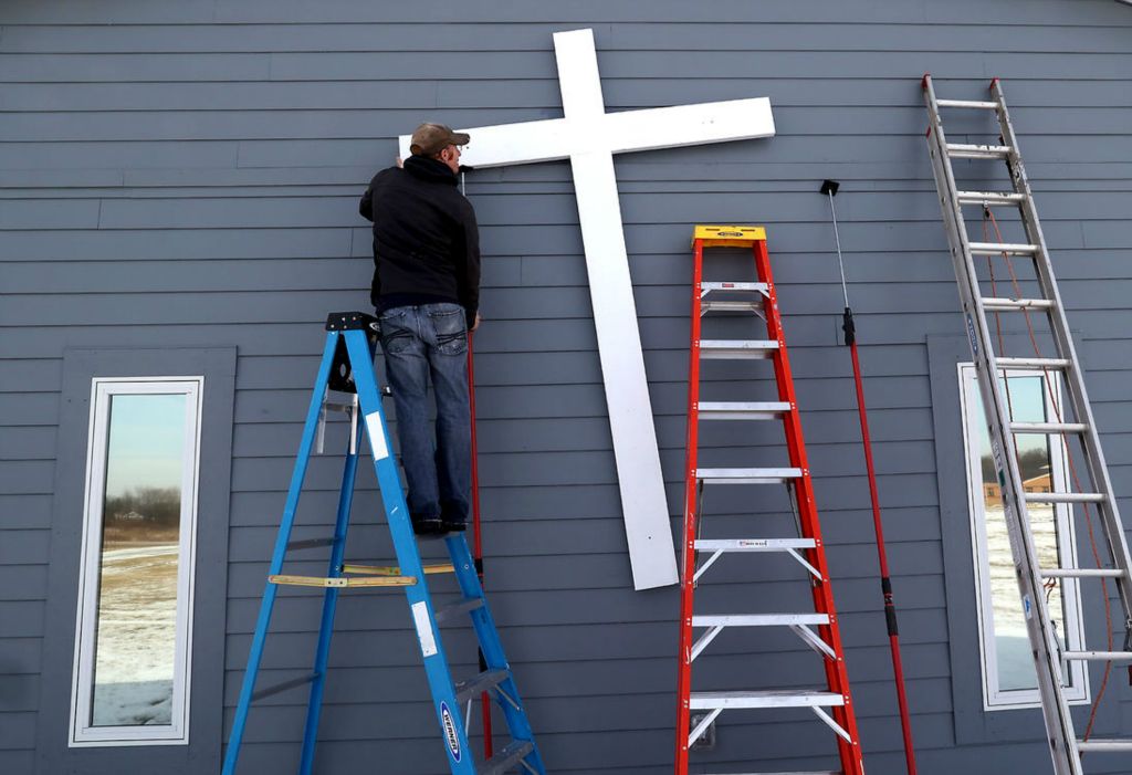 Feature - HM - Kyle Williamson straightens the cross that he and his father, Jack, were hanging on the front of the St. Paris First Church of God along US 36. (Bill Lackey / Springfield News-Sun)