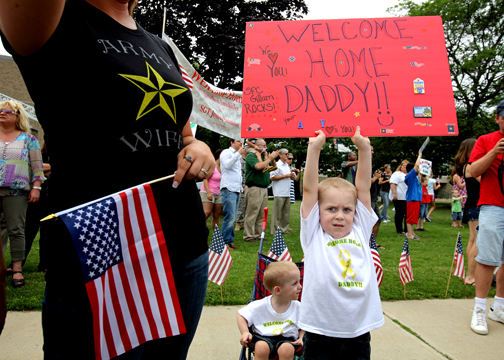 General News - 3rd place - Aydan Gillum, 5, (right) of Brunswick, stands on his tippy toes so his dad could see his sign as his dad pulls up in a bus during a welcome home ceremony for the 112th Engineer Battalion at the Lakewood Civic Auditorium. Aydan is watching his father, SFC Brian Gillum of the 112th Engineer Battalion (Task Force Predator), come home for the first time since Christmas of last year. On left is Aydan's mother Katie Gillum (Brian's wife). (Lisa DeJong / The Plain Dealer)