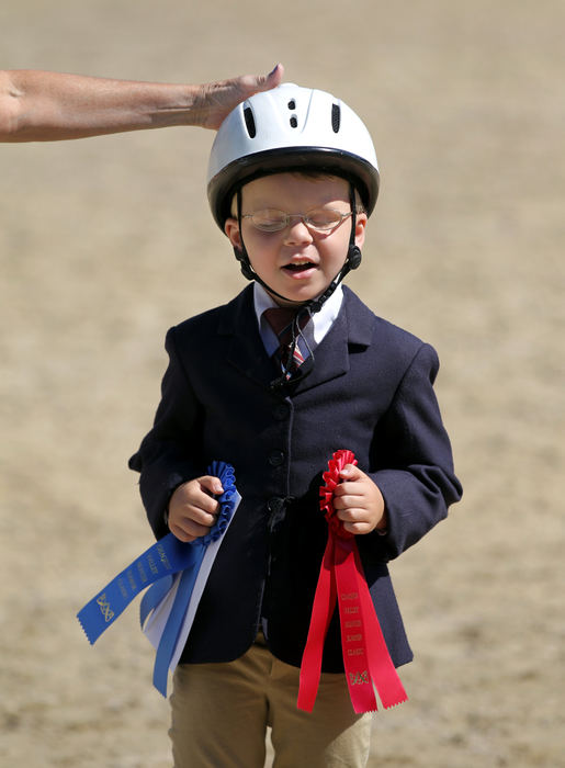 Feature - HMDylan LeMaster, 6, of Leroy, Ohio, who is mostly blind,  clutches his two ribbons as someone pats him on the head in congratulations after placing first in the category  "Beginner Equitation" and placing second in "Beginner Trail" horse riding competition during the Riders With Disabilities Horse Show hosted by Fieldstone Farm Therapeutic Riding Center at the Polo Field in Moreland Hills .   (Lisa DeJong  / The Plain Dealer)