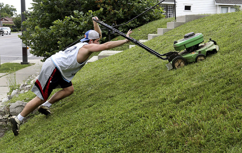 Feature - HM - A light mower and a pair of cleats makes this job doable, according to Clayton Preston, of Columbus. He and his partner, Austin Kobbeman (not pictured), of Clintonville, have their own business, PrestoKobbe Home and Lawn Care. They were working on the hillside lawn of some apartments along N. High St. at E. Kelso Rd. in Columbus. Preston handled the mowing while Kobbeman worked with the weed whacker.  (Fred Squillante / The Columbus Dispatch)