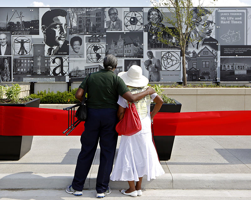 General News - 1st place - Monique Mapp (left) hugs her mother Gwendolyn Macon-Beck as they look at her sons photo on the Long Street bridge mural during the unveiling event.  Mapp's son was a part of the Urban String Youth Orchestra photo to the upper middle left of the tree.  (Kyle Robertson / The Columbus Dispatch)