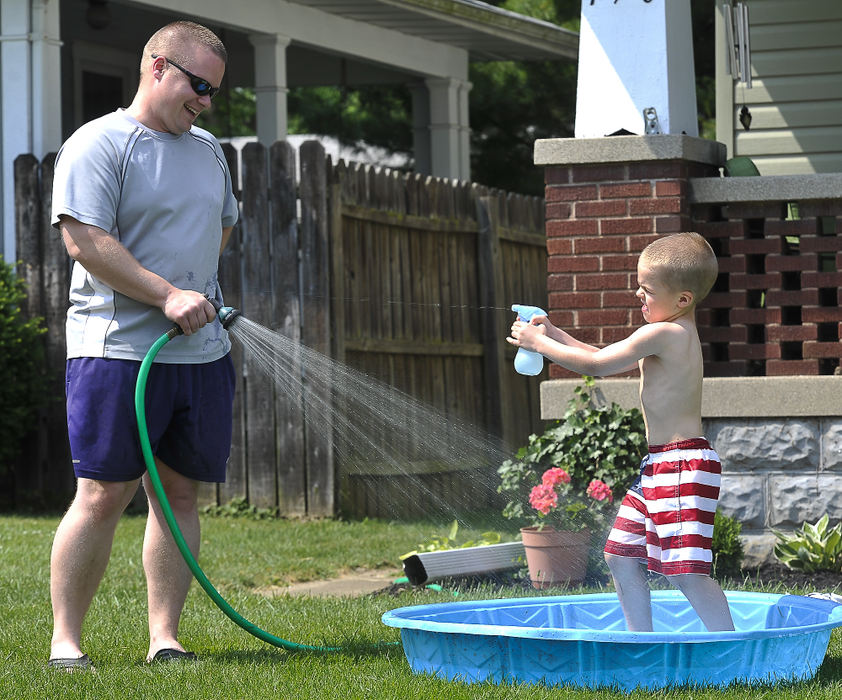 Feature - HMBen Ganson gets squirted by his son, Micah, 5, as he fills up his kiddie pool with a garden hose in the family's front yard. (Bill Lackey / Springfield News-Sun)