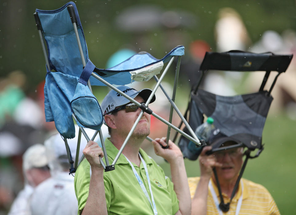 Feature - 1st placeKevin Labitzke sacrificed a dry seat for a dry head when the rains began during the second day of play the Memorial Tournament at Muirfield Village Golf Club.  His father Don Labitzke is behind him and is using his chair as an umbrella.  (Chris Russell / The Columbus Dispatch )