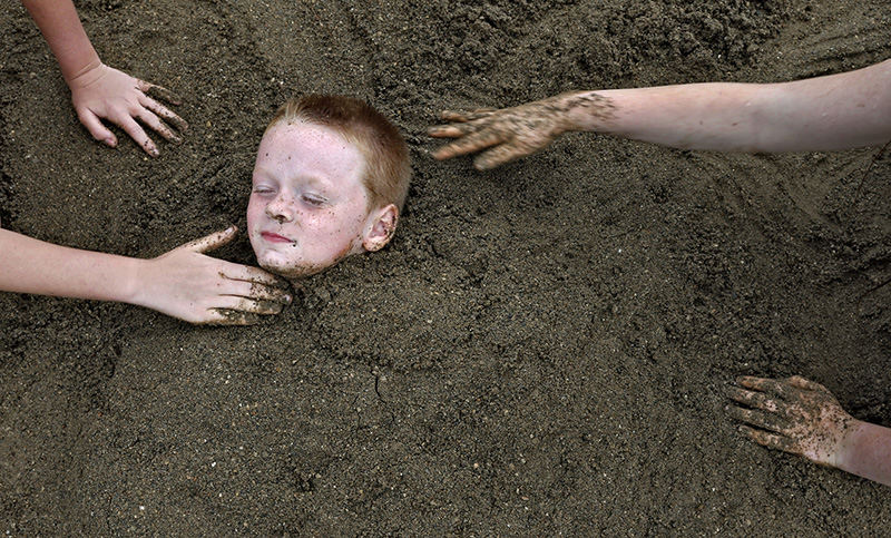 Feature - 3rd place - Showing a lot of trust in his sisters , Anthony Waddle gets buried up to his neck while playing at Alum Creek State Park with his sisters Cameron Malfe, and Halie Waddle.  Recent rains made the sand perfect for the burial task at hand.  (Chris Russell / The Columbus Dispatch)