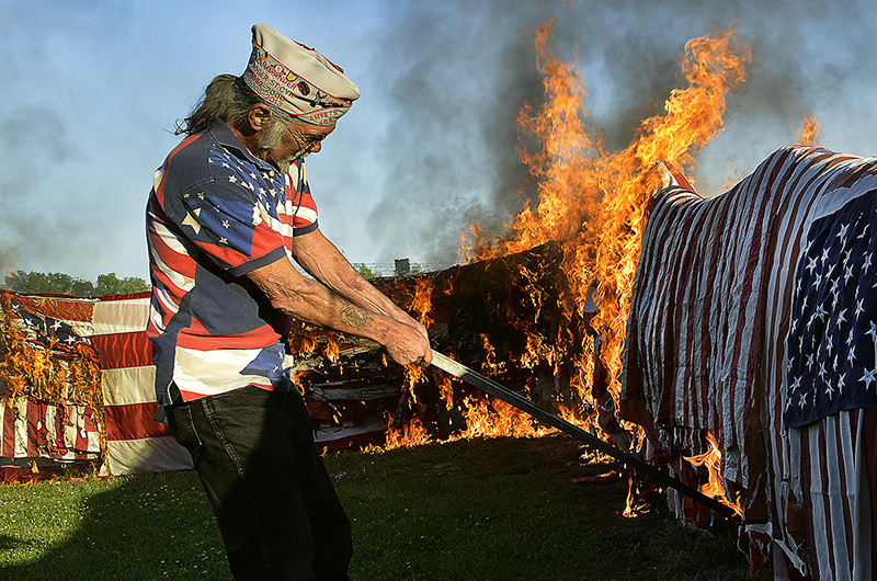 General News - 1st place - Roger St. Cyr walks along the wall of American flags setting fire to them with a crutch during the 26th Flag Day flag retirement ceremony at the American Legion Post 286 in New Carlisle. During this year's ceremony, more than 5,000 worn out and faded flags were destroyed.  (Bill Lackey / Springfield News-Sun)