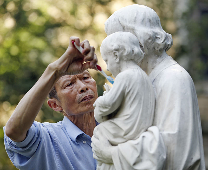 Feature - HM - Khoan Nguyen of Columbus cleans the Saint Joseph statue with a toothbrush outside Saint Joseph Cathedral in Columbus.  Nguyen who is retiring at the end of July and moving to California was cleaning the statue for the first time in 20 years.  (Kyle Robertson / The Columbus Dispatch)