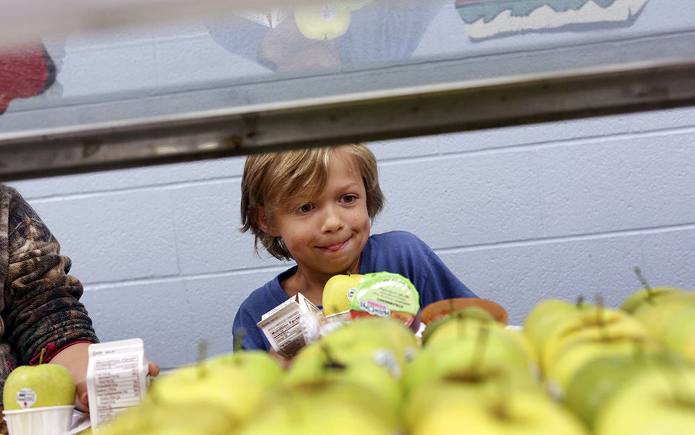 MT General News - 1st place - Cash White balances his plate during lunch while getting a apple at Mt. Logan Elementary School in Chillicothe. The school teaches summer skills classes and offers lunch to the students attending.The Children's Hunger Alliance has helped fund a summer program in the southern region of Ohio to help reduce food insecurity. (Eric Albrecht / The Columbus Dispatch)