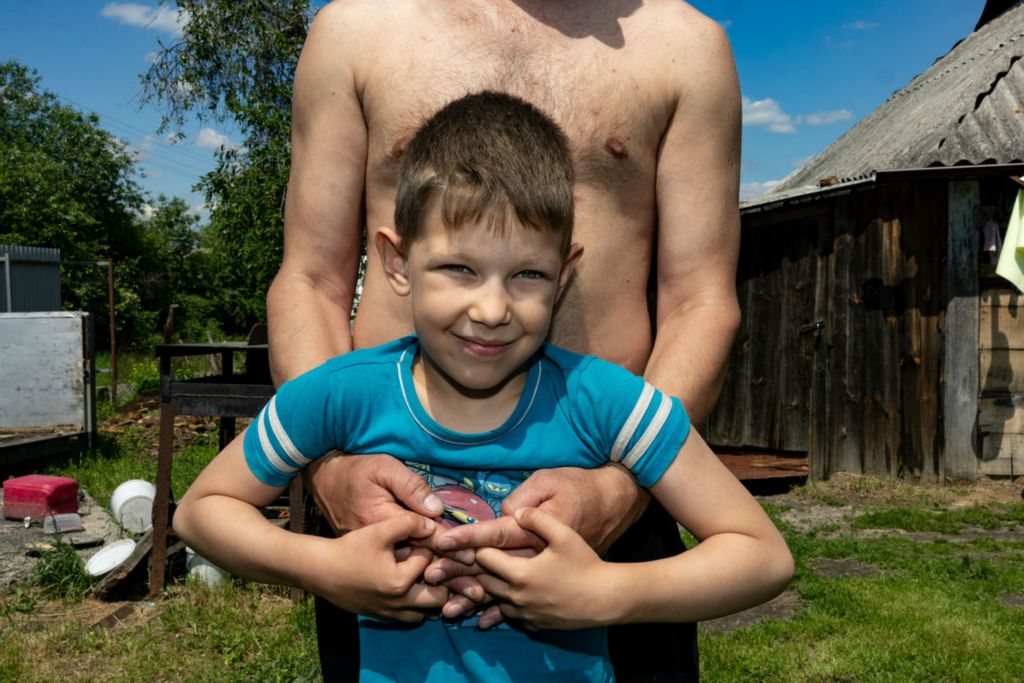 Portrait - 3rd place - Alexander Goray, 36, holds Daniel Goray, 8, in front of their home in Katiuzhanka, Ukraine on Friday June 3, 2022. The Goray family survived Russian occupation of their community over a number of days, utilizing their garden for a source of food and coordinating with neighbors. (Stephen Zenner / The Blade)