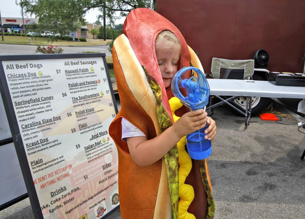 Feature - 1st place - Briella Setzer looked like a hot hotdog as she uses a handheld fan to keep cool in her hotdog costume. Briella was dressed like a hotdog to attract business to her family's hotdog cart called Briella's Hotdogs which was parked in a parking lot along North Bechtle Avenue.  (Bill Lackey / Springfield News-Sun)