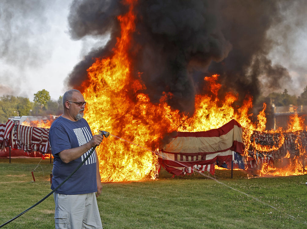 General News - 1st place - Tony Rieker extinguishes extinguishes a small grass fire after helping light thousands of American flags during the annual flag retirement ceremony at American Legion Post 286 in New Carlisle. The American Legiion receives thousands of faded and worn out flags from all over the country to officially retire. This year they retired between 8,000 - 10,000 flags.  (Bill Lackey / Springfield News-Sun)