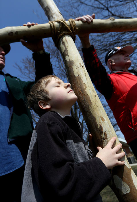 General News - HMRicky Schlotzhauer squints into the sunlight while others help to support the cross during a stop on the Multi-Denominational Stations of the Cross event at the Johnstown Village offices. The stations of the cross involves community members carrying a large cross to remember the experience of Jesus walking to his crucifixion. The tour included several area churches, the local firehouse and a spot on the town hall square. Each stop included singing, prayer and time for reflection.  (Brooke LaValley / The Columbus Dispatch)