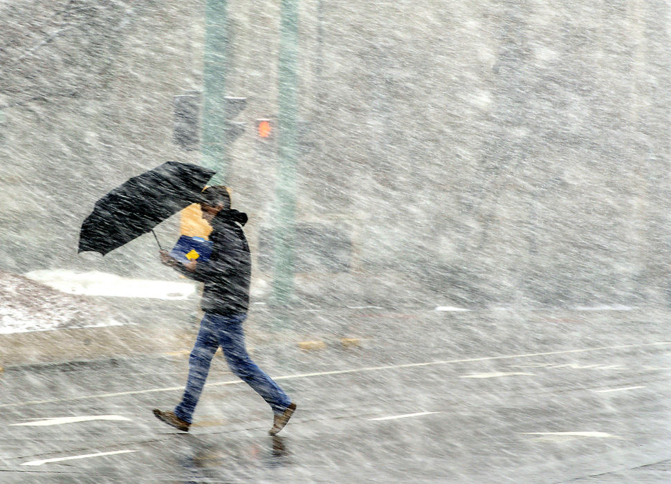 Feature - HM - A pedestrian dashes through the heavy snow as he crosses Limestone Street in downtown Springfield with an umbrella. (Bill Lackey / Springfield News-Sun)