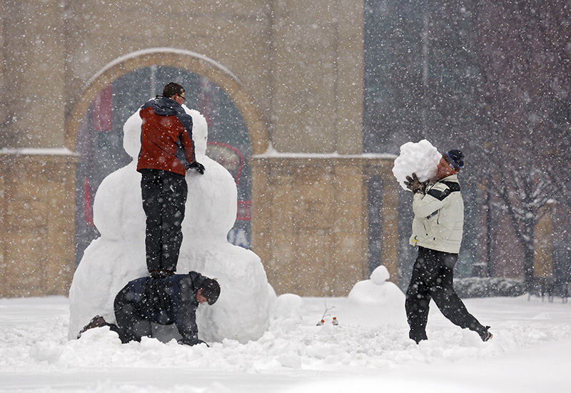 Feature - 2nd place - Iran McRae stands atop his brother Sean McRae while their father Charles McRae brings on more snow for the snowman they were building at McFerson Commons in the Arena District where they live. It took two hours and their motivation they said was the snow was very packable.  (Eric Albrecht / The Columbus Dispatch)