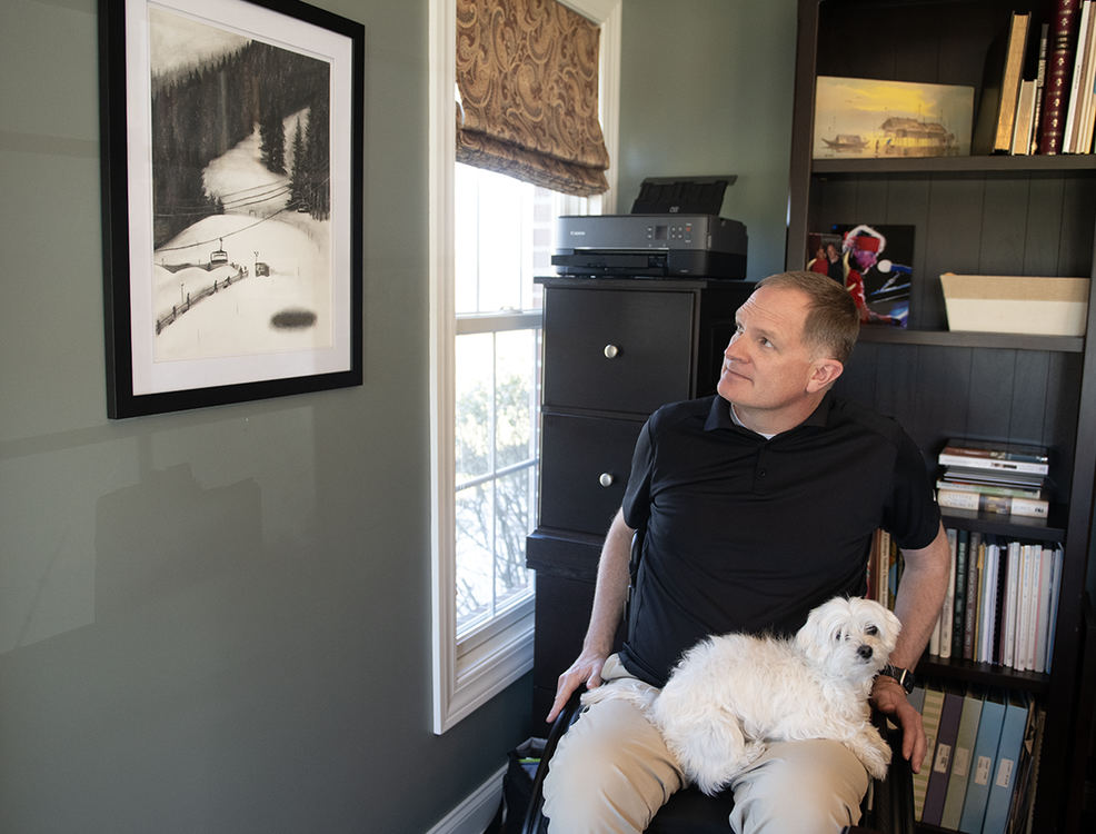 Story - 2nd place - Jason Kolb, at his home office in Stow, looks at a charcoal drawing by Tera Deetscreek called "Sacred Ground" which is a depiction of the exact spot Kolb had his ski accident. Daisy, the family's 4-year-old Coton de Tulear, sits on Jason's lap. (Lisa Scalfaro / Akron Beacon Journal)