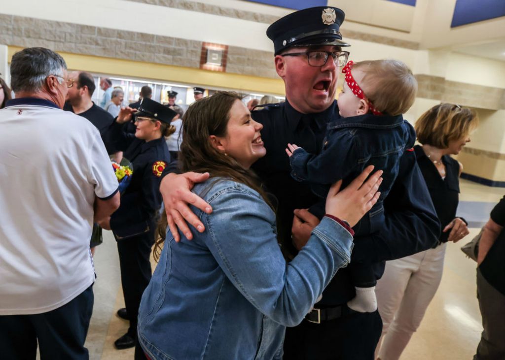 General News - 1st place - Maumee resident Wendy Waisner, from left, laughs as her husband Denton Waisner, a newly graduated member of Fire Class 295, makes faces to the amusement of their daughter Amelia Waisner, age 10 months, following a graduation ceremony on Friday, May 20, 2022 at Bowsher High School in Toledo.  (Isaac Rithcey - The Blade)  