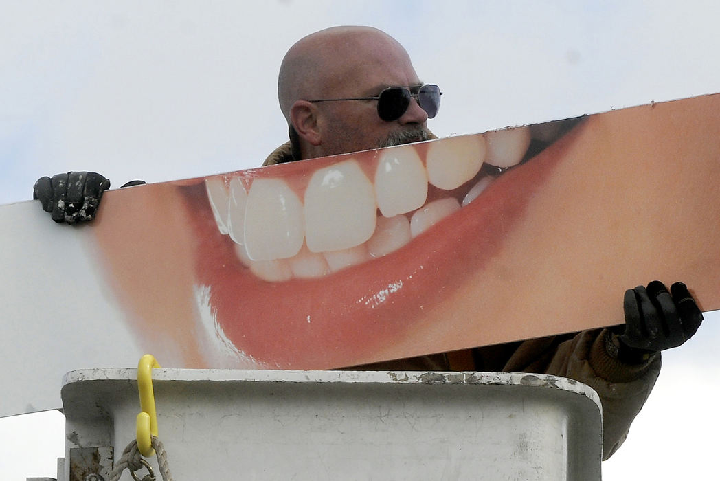 Feature - 1st place - Steve McQuistion, an employee of Sign Affects, looks like he's showing off his oversized pearly whites as he hangs a dentist sign at the Tower Building in Springfield. (Marshall Gorby / Springfield News-Sun)