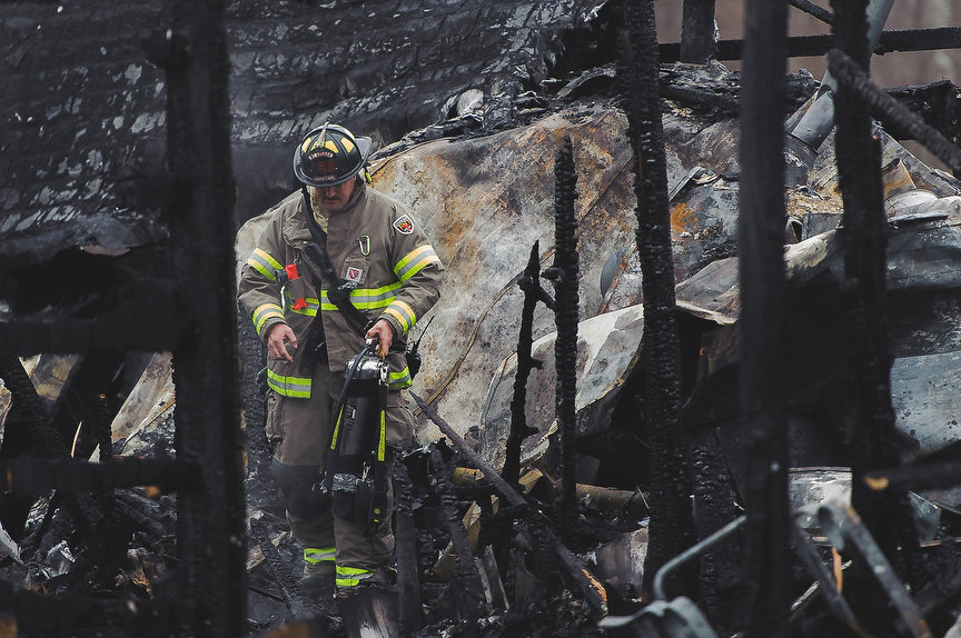 Spot News - 2nd place - Mount Vernon firefighter Coty Shellenbarger extinguishes a rekindled fire on Upper Fredericktown Road. A woman was killed in the house fire. The cause of the fire is unknown and remains under investigation. (Joshua Morrison / Mount Vernon News)