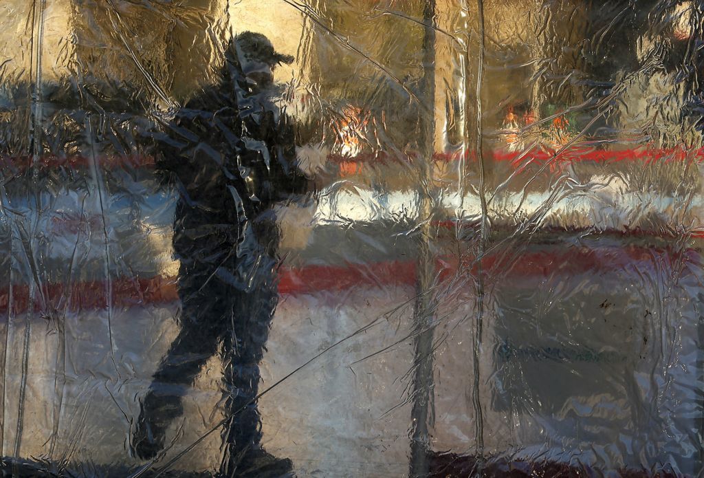 Feature - HM - A worker is seen through a wrinkly, clear, plastic tarp as he sets up the temporary ice skating rink on the Springfield City Hall Plaza. (Bill Lackey / Springfield News-Sun)