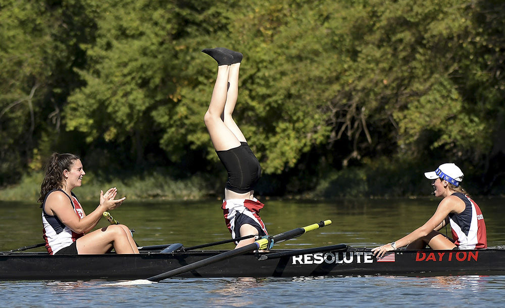 Sports Feature - 3rd place - Hannah Butler does a headstand in Dayton's Varsity 8 boat "resolute" while teammates, Madison Conway (right) and Meghan Garriot cheer her on. The Dayton Flyers rowing team was on the Great Miami River in Moraine, Ohio practicing for an upcoming regatta.  (Erik Schelkun / Elsestar Images)