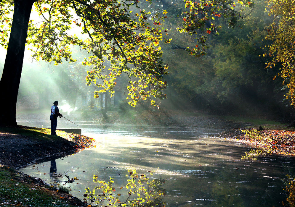 Feature - HM - Sunlight streaks through the fog on a chilly morning as a man fishes in the Snyder Park Lagoon.  Bill Lackey / Springfield News-Sun