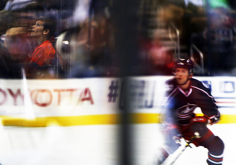 spoSports Feature - 1st place - A fan is reflected watching the Columbus Blue Jackets as defenseman Jaime Sifers looks for the puck during the preseason game against Minnesota Wild at Nationwide Arena. Sifers, formerly on Minnesota Wild, signed with the Jackets for two-years this season.  (Leah Klafczynski / The Columbus Dispatch)