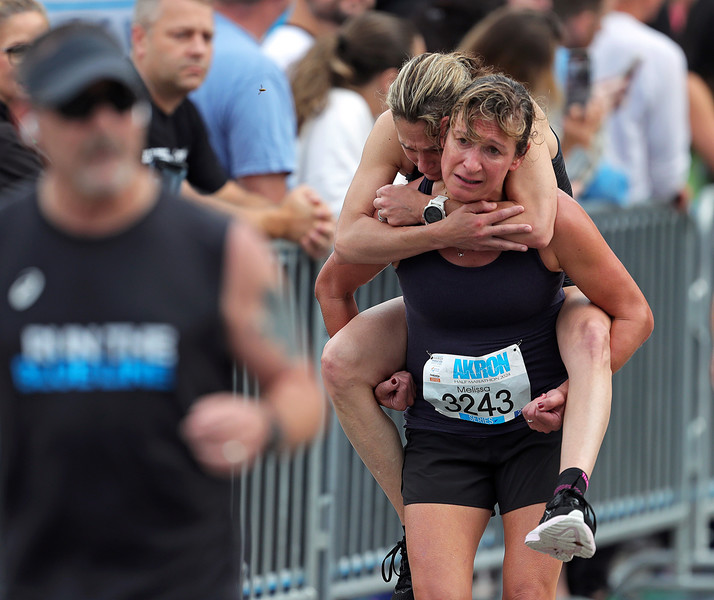 Sports - 2nd place - Melissa Owen of North Canton helps another runner make it to the finish during the 2024 Akron Half Marathon. (Jeff Lange / Akron Beacon Journal)