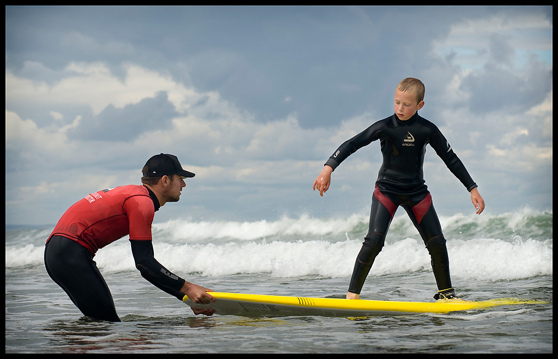 Larry Fullerton Photojournalism Scholarship - James Roh / Ohio UniversityNiall Shiells helps a student, Jack Gray, learn how to balance on his surfboard in the water at Belhaven beach in Belhaven, Scotland.