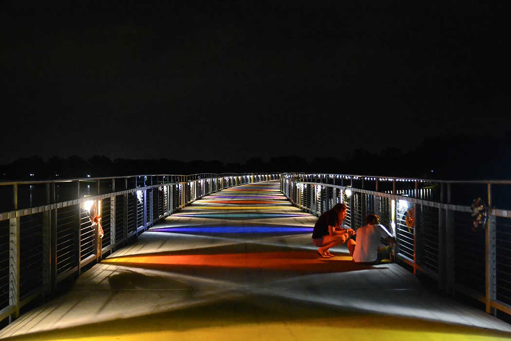 Second Place, Larry Fullerton Photojournalism Scholarship - Madison Schmidt / University of CincinnatiGray's Lake Park in Des Moine, Iowa features a colorful lit bridge that seems to wrap in and out of site. A couple stopped and bent down to examine one of the many orb weaver spiders that build their flat spiral webs near each of the lights on the bridge.