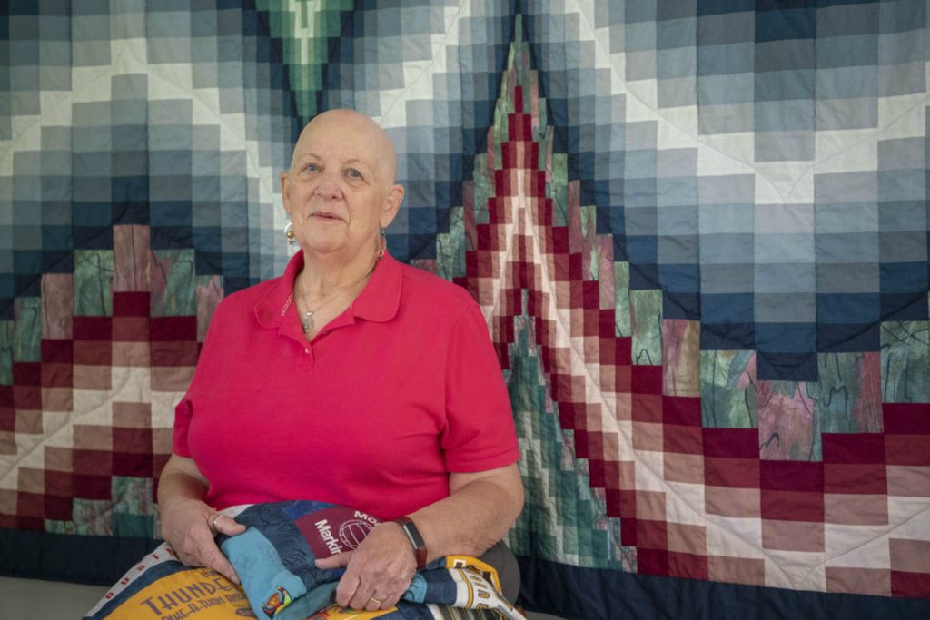 Second Place - Larry Fullerton Photojournalism Scholarship , Grace Wilson / Ohio UniversityJeannette Fromm, 75, of Centerville, sits in front of a quilt she made, while holding another quilt, made for her husband out of his college t-shirts, on Sept. 13, 2020.  Jeannette began sewing when she was in sixth grade, she made herself a pair of shorts. Her talent of sewing and quilting has developed in a passion and a way to give back to her community. "I don't really truly have many quilts I've made; I give them all away."