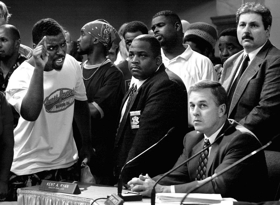 First Place, News Picture Story - Steven M. Herppich / Cincinnati EnquirerAlmost two hundred protestors crowd around city council members as an angry Ronnie Stallworth yells at Cincinnati Police Chief Tom Streicher during a hearing of the law committee at City Hall in Cincinnati following the killing of Timothy Thomas, an unarmed African American, by police officer Steven Roach two days earlier. The shooting lead to one week of protests, riots, and a city imposed curfew leading up to the funeral of this 19-year-old man.