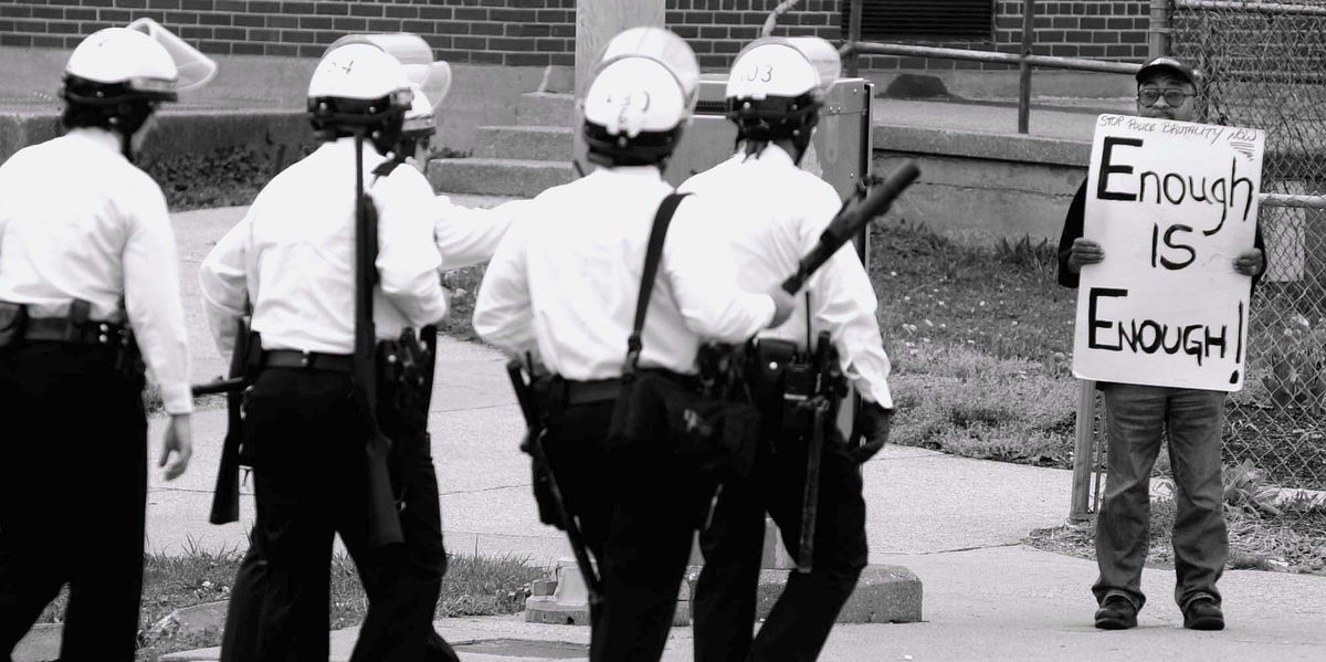 Second Place, News Picture Story - Michael E. Keating / Cincinnati EnquirerAs a riot squad of police move into a neighborhood a lone protestor stands on a street corner in silent protest of alleged police abuses. Questions of police training and actions launched a US Dept. of Justice investigation.