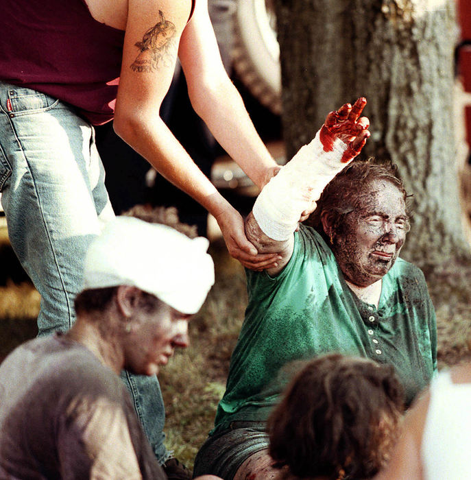 Third Place, News Picture Story - Shirley Ware / The Medina GazetteSunday July 29th, 2001 an antique steam engine exploded at the Medina County Fairgrounds. A malfunction in the steam engine of a 1918 Case tractor caused it to become a bomb that strewed shrapnel, steam and boiling water over the fair goers. 5 people died and 50 were injured including 2 police officers. Minutes after the explosion a victim is helped by a young man as they wait for paramedics to transport her to the hospital burn unit.